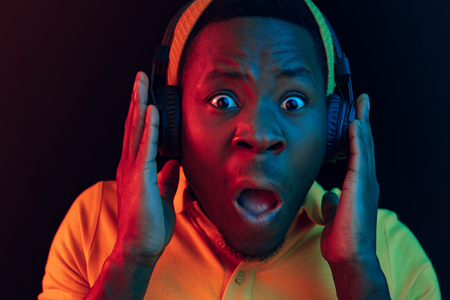 The young handsome happy hipster man listening music with headphones at black studio with neon lights. Disco, night club, hip hop style, positive emotions, face expression, dancing conceptの写真素材