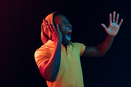 The young handsome happy surprised hipster man listening music with headphones at black studio with neon lights. Disco, night club, hip hop style, positive emotions, face expression, dancing conceptの写真素材