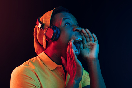 The young handsome happy hipster man listening music with headphones at black studio with neon lights. Disco, night club, hip hop style, positive emotions, face expression, dancing conceptの写真素材