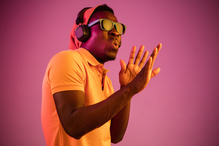 The young handsome serious sad hipster man listening music with headphones at studio with neon lights. Disco, night club, hip hop style, positive emotions, face expression, dancing conceptの写真素材