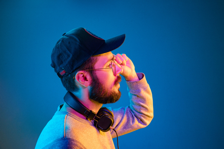 Enjoying his favorite music. Happy young stylish man in sunglasses with headphones smiling while standing against blue neon backgroundの写真素材