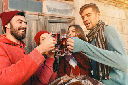 Smiling european men and women during party photoshoot. The guys posing as friends at studio fest with wineglasses with hot mulled wine on foreground.の写真素材