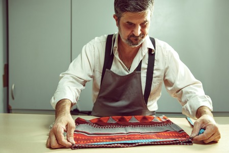 Closeup of tailors table with male hands tracing fabric making pattern for clothes in traditional atelier studio. The man in female profession. Gender equality conceptの写真素材