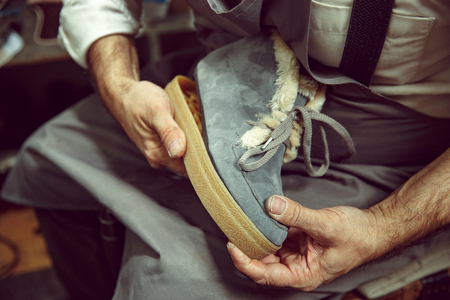 Enjoying process of creation custom made shoes. Workplace of shoe designer. Hands of shoemaker dealing with cobbler tool, close upの写真素材