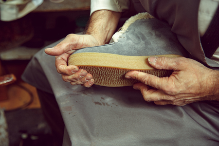 Enjoying process of creation custom made shoes. Workplace of shoe designer. Hands of shoemaker dealing with cobbler tool, close upの写真素材