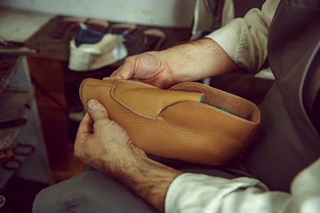 Enjoying process of craft shoes creation. Workplace of shoe designer. Hands of shoemaker dealing...
