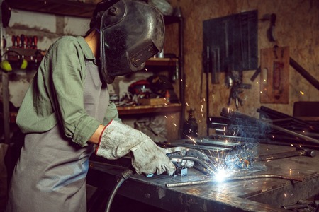 Busy and serious craftswoman grinding timbers with special machine. Beautiful woman wearing safety...