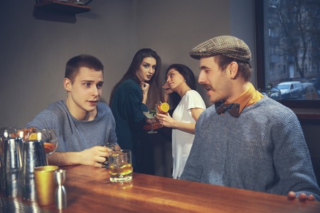 Two young men in casual clothes talking while sitting at bar counter in pubの写真素材