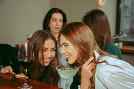 Female friends having a drinks at bar. They are sitting at a wooden table with cocktails. They are...