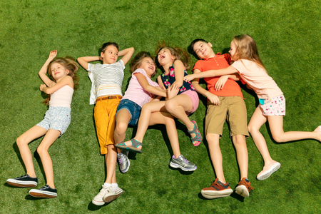 Group of happy children playing outdoors. Kids having fun in spring park. Friends lying on green...