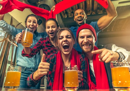Sport, people, leisure, friendship, entertainment concept - happy male and female football fans or good young friends drinking beer, celebrating victory at bar or pub. Human positive emotions conceptの写真素材