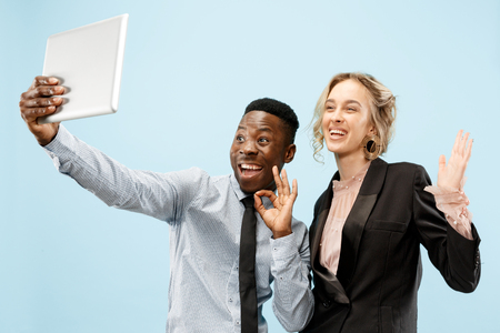 Concept of partnership in business. Young happy smiling man and woman standing with tablet against blue background at studioの写真素材