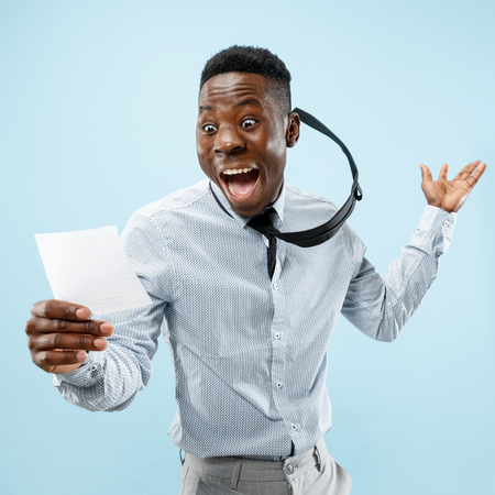 Young afro man with a surprised happy expression won a bet on blue studio background. Human facial emotions and betting concept. Trendy colorsの写真素材