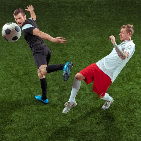 Football player tackling for ball over green grass background. Professional male soccer players in...