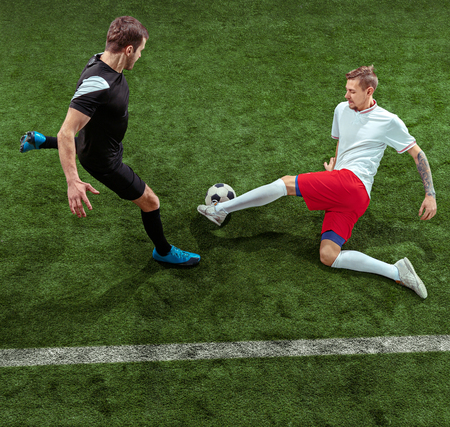 Football player tackling for ball over green grass background. Professional male soccer players in motion at stadium. Fit jumping men in action, jump, movement at game.の写真素材