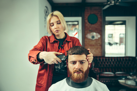 Client during beard shaving in barbershop. Female barber at salon. Gender equality. Woman in the male profession.の写真素材