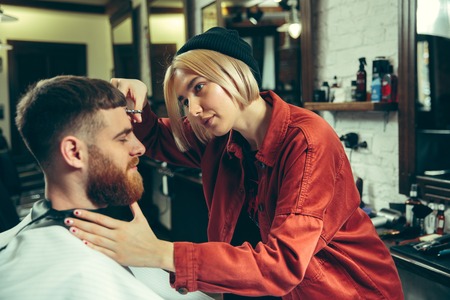 Client during beard shaving in barbershop. Female barber at salon. Gender equality. Woman in the male profession.の写真素材