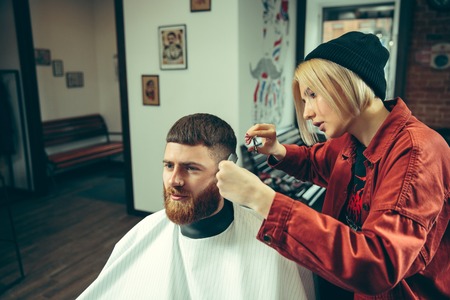 Client during beard shaving in barbershop. Female barber at salon. Gender equality. Woman in the male profession.の写真素材