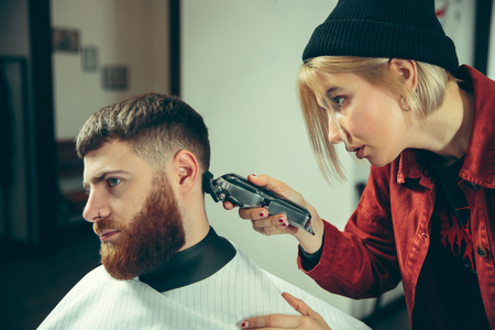 Client during beard shaving in barbershop. Female barber at salon. Gender equality. Woman in the male profession.の写真素材
