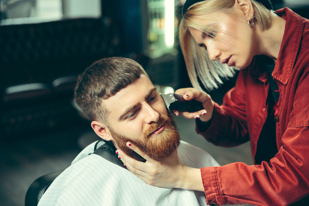 Client during beard shaving in barbershop. Female barber at salon. Gender equality. Woman in the male profession.の写真素材
