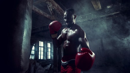 Hands of boxer over dark gym background. Strength, attack and motion concept. Fit african american...