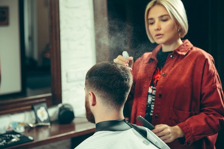 Client during beard shaving in barbershop. Female barber at salon. Gender equality. Woman in the...