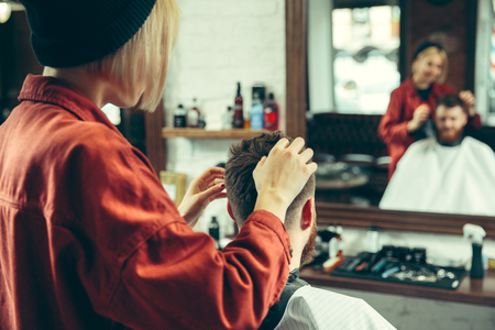 Client during beard shaving in barbershop. Female barber at salon. Gender equality. Woman in the male profession.の写真素材