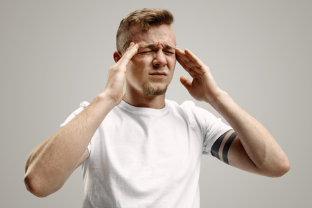 Man having headache. Business man standing with pain isolated on gray studio background. Male half-length portrait. Human emotions, facial expression conceptの写真素材