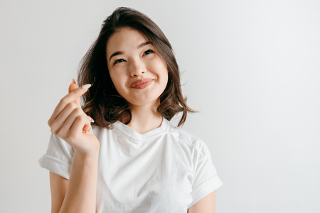 Happy asian woman standing and smiling isolated on gray studio background. Beautiful female half-length portrait. Young emotional woman. The human emotions, facial expression concept.の写真素材