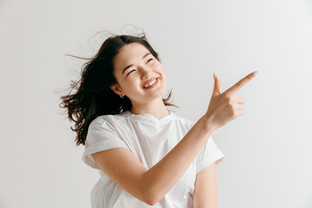 Happy asian woman standing and presenting something isolated on gray studio background. Beautiful female half-length portrait. Young emotional woman. The human emotions, facial expression concept.の写真素材