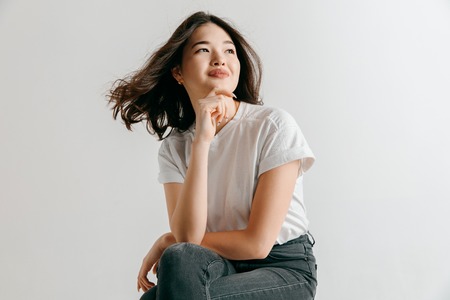 Happy asian woman standing and smiling isolated on gray studio background. Beautiful female...