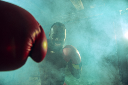 Hands of boxer over dark gym background. Strength, attack and motion concept. Fit african american model in movement. Naked muscular athlete in red gloves. Sporty man during boxing.の写真素材
