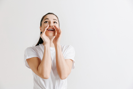 Do not miss. Young casual woman shouting. Shout. Crying emotional woman screaming on gray studio background. Female half-length portrait. Human emotions, facial expression concept.の写真素材