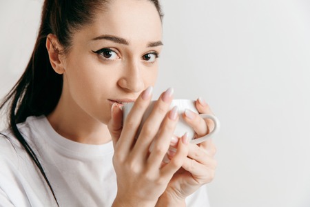 Taking a coffee break. Handsome young man holding coffee cup while standing against gray studio background.の写真素材