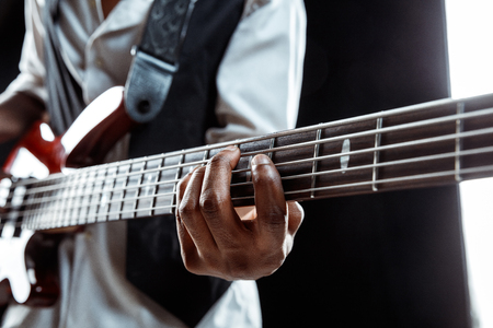 African American handsome jazz musician playing bass guitar in the studio on a black background. Music concept. Young joyful attractive guy improvising. Close-up retro portrait.の写真素材