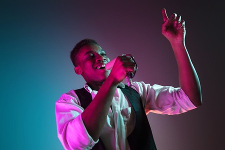 African American handsome jazz musician singing into the microphone in the studio on a neon background. Music concept. Young joyful attractive guy improvising. Close-up retro portrait.の写真素材