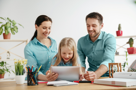 Father, mother and their daughter are smiling while spending time together. A day with family. Young happy couple with child are studying with the tablet. Education, studying and knowledge sharing concept.の写真素材