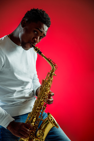 African American handsome jazz musician playing the saxophone in the studio on a neon background. Music concept. Young joyful attractive guy improvising. Close-up retro portrait.の写真素材