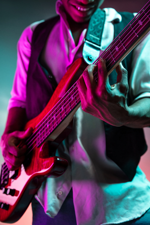 African American handsome jazz musician playing bass guitar in the studio on a neon background. Music concept. Young joyful attractive guy improvising. Close-up retro portrait.の写真素材