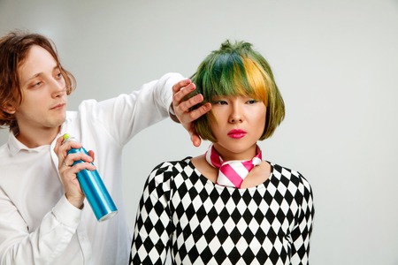 Picture showing adult woman at the hair salon. Studio shot of graceful young girl with stylish short haircut and colorful hair on gray background and hands of hairdresser.の写真素材