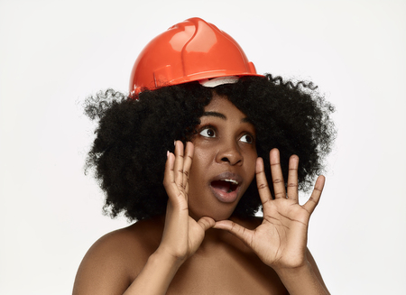 Portrait of confident female african american happy smiling worker in orange helmet. Woman isolated on white studio backgrouns. Beauty, cosmetics, skincare, skin and facial protection, cosmetology and cream conceptの写真素材
