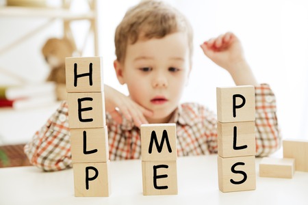Wooden cubes with words HELP ME PLS in hands of little boy at home. Conceptual image about education, childhood and social problems.の写真素材