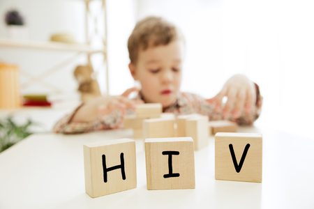 Wooden cubes with word HIV in hands of little boy at home. Symbol of the fight against AIDS and cancer. Concept of helping those in needの写真素材