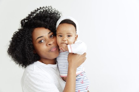 Closeup portrait of beautiful african woman holding on hands her little daughter on white...