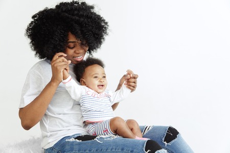 Closeup portrait of beautiful african woman holding on hands her little daughter on white...