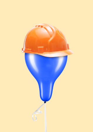 A light and aerial safety. A blue balloon with orange consrtuction helmet and against yellow background. Negative space to insert your text. Business concept. Modern design. Contemporary art collage.の写真素材
