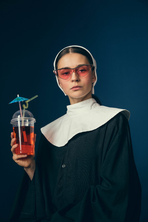 Medieval pub or summer resort. Young woman as a nun in vintage clothing and white mutch sitting on...