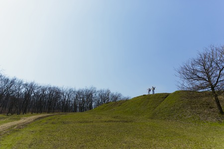 Wanderers in a big world. Aged family couple of man and woman in tourist outfit walking at green lawn near by trees in sunny day. Concept of tourism, healthy lifestyle, relaxation and togetherness.の写真素材