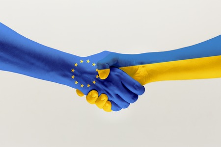 Welcome gesture. Two male hands shaking colored in flag of European Unity and Ukraine isolated on grey studio background. Concept of help, partnership of countries, political and economical relations.の写真素材