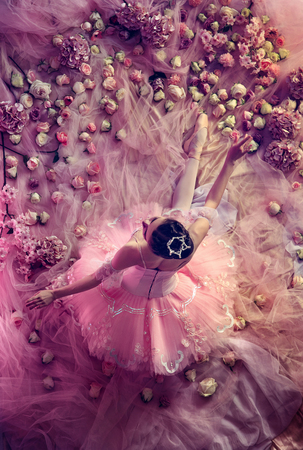 Smell of roses.Top view of beautiful young woman in pink ballet tutu surrounded by flowers. Spring mood and tenderness in coral light. Art photo. Concept of spring, blossom and natures awakening.の写真素材